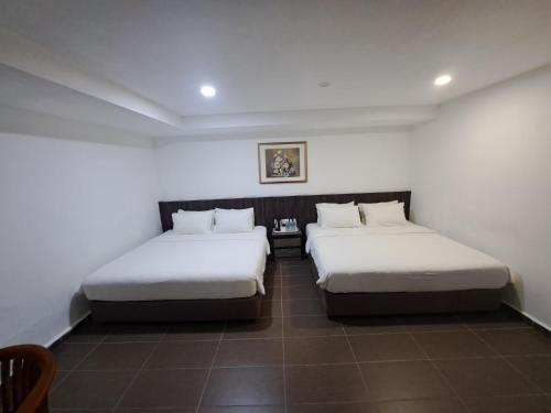 two beds in a room with white walls at Hotel Al Abraar in Melaka
