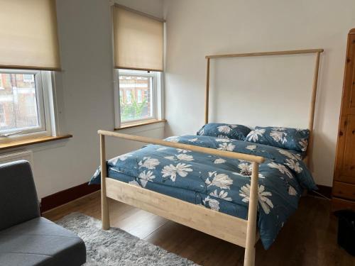 a bedroom with a bed with a blue comforter and two windows at Honor Oak Park Homestay in London