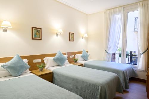 Habitación de hotel con 3 camas con almohadas azules en Pensión San Jerónimo, en San Sebastián