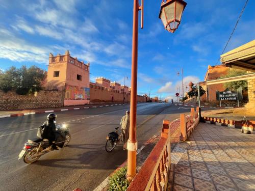 two people riding motorcycles down a street with a street light at Hotel Restaurant La Kasbah in Tinerhir