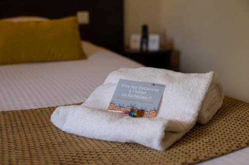 a towel with a book on it sitting on a bed at Logis Hotel Le Richelieu - Royan Atlantique in Saujon