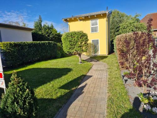 a garden with a yellow house and a sidewalk at Ferienhaus an der Brunnenaue 4 Sterne, E-Ladestation am Haus, Wlan, Netflix, Garten in Sagard