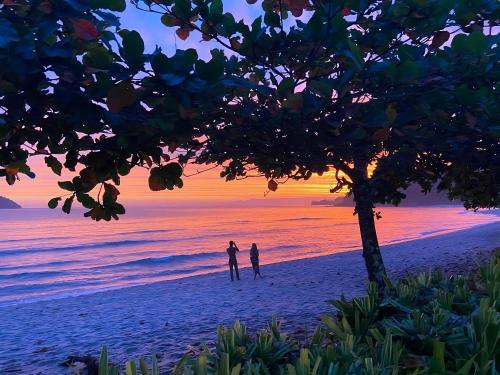two people standing on the beach at sunset at Suítes Pé na Areia in Barra do Sahy