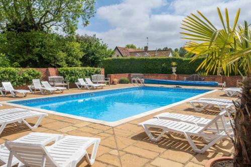 - une piscine bordée de chaises longues blanches dans l'établissement East Green Farm Cottages - The Granary, à Saxmundham