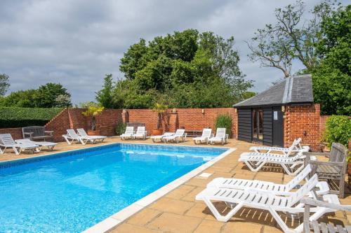 une piscine avec des chaises longues et un bâtiment dans l'établissement East Green Farm Cottages - The Granary, à Saxmundham