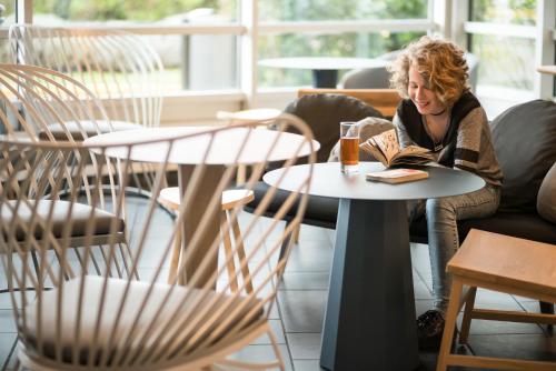 a woman sitting at a table reading a book at Novotel Suites Paris CDG Airport Villepinte in Roissy-en-France