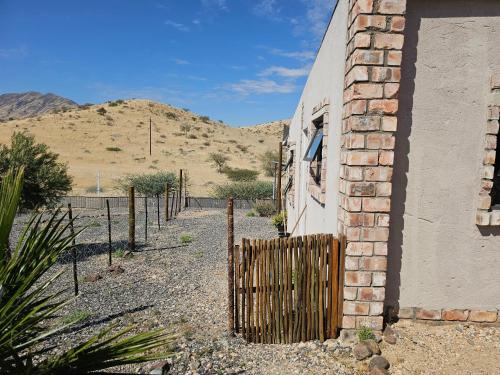 a brick building with a fence and mountains in the background at Carlo's Mountain Lodge in Usakos