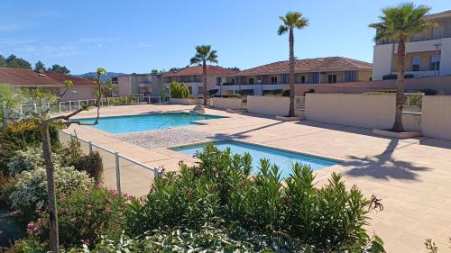 une piscine dans une cour avec des palmiers dans l'établissement Résidence les Parasols d'Argens, à Roquebrune-sur Argens