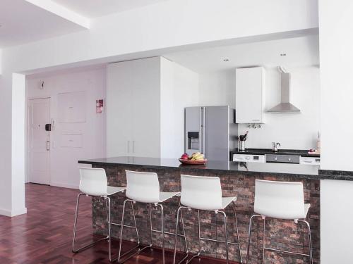 a kitchen with white cabinets and a counter with white chairs at casaRene in Carcavelos