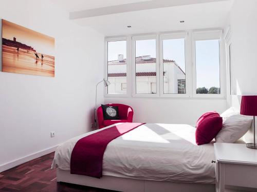 um quarto branco com uma cama e uma cadeira vermelha em casaRene em Carcavelos