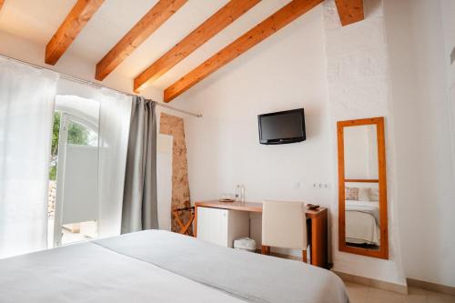 a bedroom with a bed and a desk and a television at Hotel Rural Binigaus Vell in Es Migjorn Gran