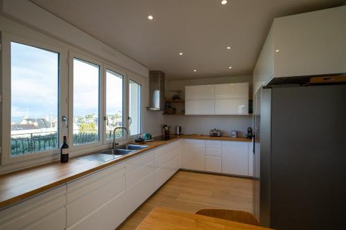 une cuisine avec des placards blancs et une grande fenêtre dans l'établissement Très belle maison avec vue sur mer, à Saint-Lunaire