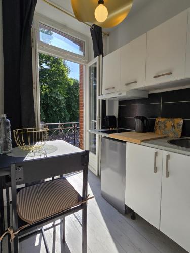 une cuisine avec des armoires blanches, une table et une fenêtre dans l'établissement Charmant appartement chambre, cuisine et salle de bain avec balcon sur Jardin Massey, à Tarbes