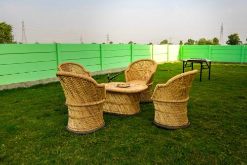 three wicker chairs and a table in the grass at Chaudhary Farm house in Daula