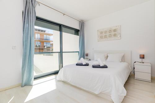 Un dormitorio blanco con una cama y una ventana grande. en Cavalo Preto Luxury Beach Apartment by Golden Zenith, en Quarteira