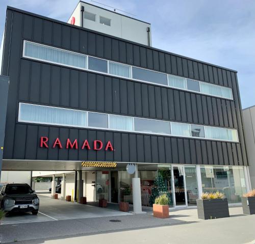 a building with a car parked in a parking lot at Ramada Suites by Wyndham Christchurch City in Christchurch