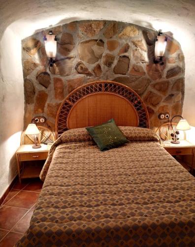 a bedroom with a large bed with a stone wall at Casa Cueva, Cuevas del Emir in Freila