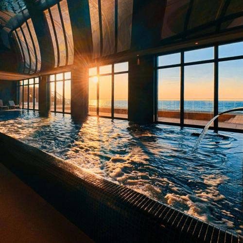 a large swimming pool with the sun shining through the windows at Sea View Smart & Garden VIP Apartment in Międzyzdroje