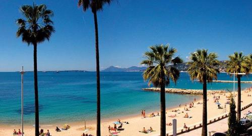 un groupe de personnes sur une plage avec des palmiers dans l'établissement JUAN - PLAGES - PARKING Privé - TERRASSE VUE MER, à Juan-les-Pins