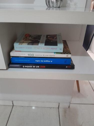 a stack of books sitting on a white shelf at Apartamento elegante a 1km do centro de Aracruz wifi gratuito garagem hacht cozinha equipada totamente individual in Aracruz