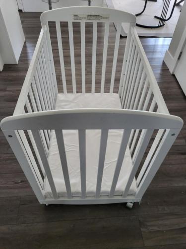 a white crib in a room with a wooden floor at Happy Zone Suite With AC- Sleeps 4- Free Welcome Snacks and Drinks ! in Langford