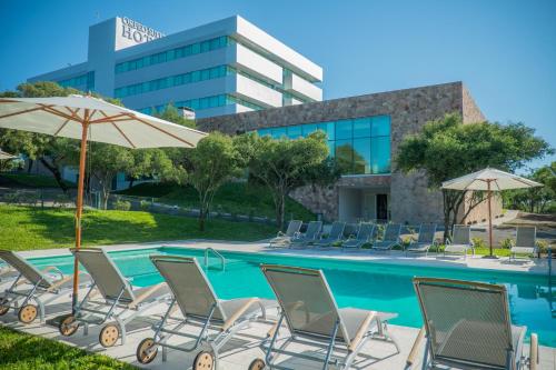 a pool with chairs and umbrellas in front of a building at Orfeo Suites Hotel Sierras Chicas in Salsipuedes