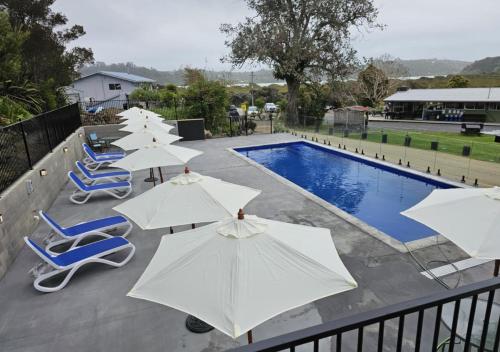 a row of white umbrellas and chairs next to a swimming pool at Russell-Orongo Bay Holiday Park in Russell