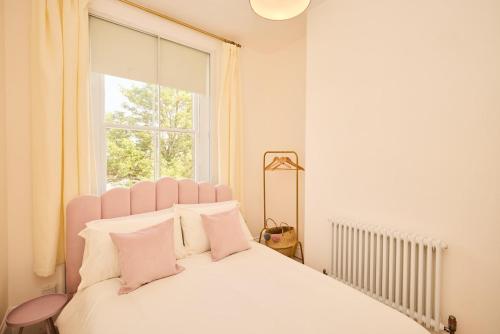 a white bed with pink pillows and a window at The Corner by the Castle in Rochester