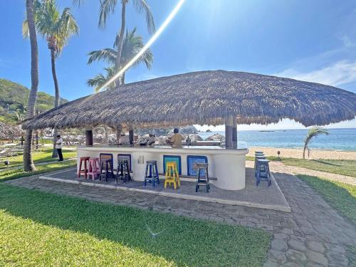 eine Strandbar mit Stühlen und Strohdach in der Unterkunft Beachfront unit with ocean view, pool, fiber optic in Bahías de Huatulco