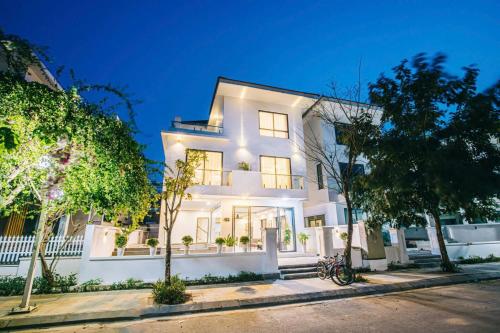 a white house with trees in front of it at Villa FLC Sầm Sơn - Cạnh Bể Bơi Vô Cực in Sầm Sơn
