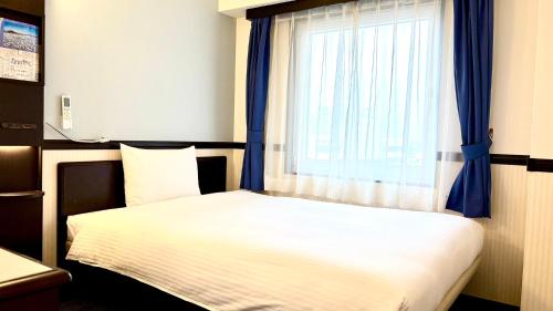 a bedroom with a bed and a window with blue curtains at Toyoko Inn Chiba Shin kamagaya Ekimae in Kamagaya