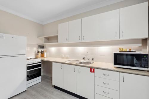 a white kitchen with white cabinets and a microwave at Smugglers On The Beach in Coffs Harbour