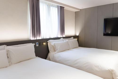 two white beds in a hotel room with a window at Talmud Hotel Classic Taiwan Boulevard in Taichung