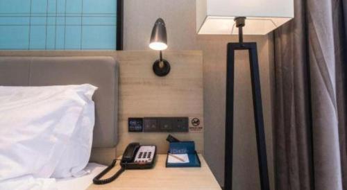 a bed with a lamp and a phone on a night stand at Echarm Hotel Hefei West Qilitang Metro Station in Hefei