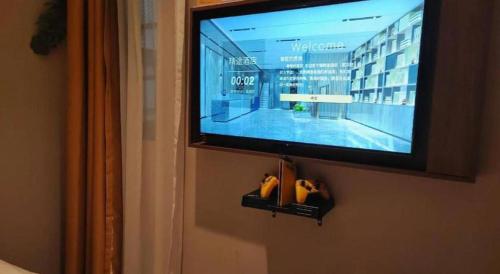 a flat screen tv hanging on a wall with shoes at JTOUR Inn Wuhan Textile University in Wuhan