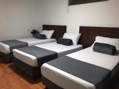 three beds in a hotel room with black pillows at Hotel Castellon Plaza Pereira in Pereira