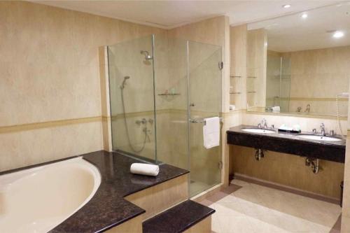 a bathroom with a tub and a shower and a sink at Grage Hotel Cirebon in Cirebon