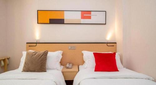 two beds in a hotel room with a red pillow at Cozy Hotel Xiamen in Xiamen