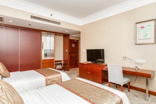 a hotel room with two beds and a desk and a television at Qingdao Blue Horizon Hotel Licang in Qingdao