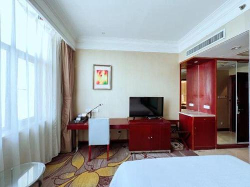 a bedroom with a desk with a television and a bed at Qingdao Blue Horizon Hotel Licang in Qingdao