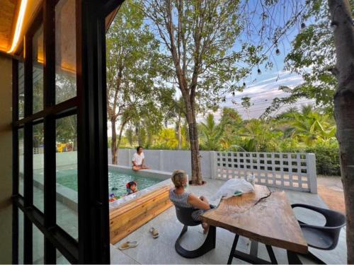 a woman sitting at a table next to a pool at The State Resort in Ban Wat Phrik
