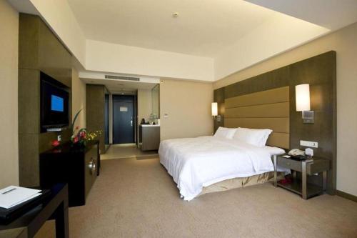 a bedroom with a large white bed and a desk at Jiaxin Conifer Hotel Shunde in Shunde
