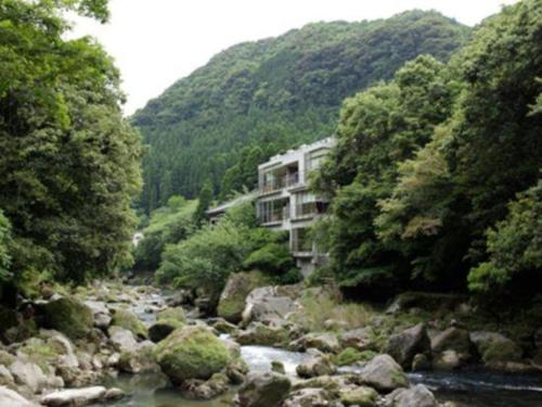 a river in front of a building next to a mountain at Myoken Ishiharaso in Kirishima