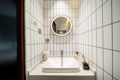 a white tiled bathroom with a sink and a mirror at Xihe Hotel-Shanghai Lujiazui Lancun Road Subway Station Branch in Shanghai