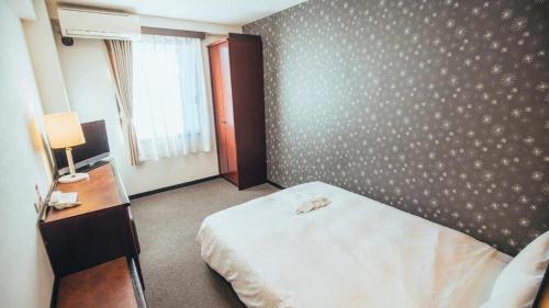 a bedroom with a bed and a desk and a window at Hotel Areaone Miyazaki in Miyazaki