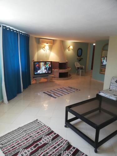 a living room with a flat screen tv and blue curtains at Villa habiba 3 chambres in El Haouaria