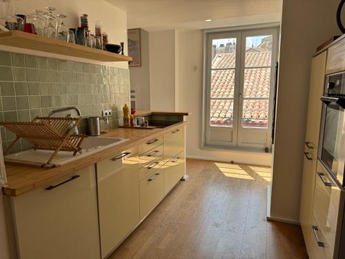 une cuisine avec des placards blancs et une grande fenêtre dans l'établissement Amaia Cœur historique de Bayonne, à Bayonne