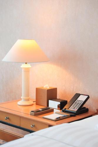 a bedside table with a lamp and a remote control at Hanoi Daewoo Hotel in Hanoi