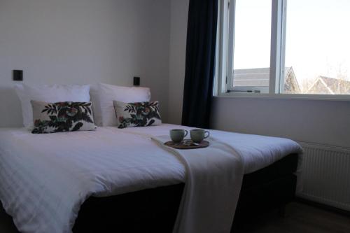 a bed with two cups on top of it with a window at Estrela Do Norte in De Cocksdorp