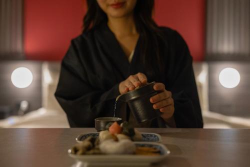 a woman sitting at a table with a cup and a plate of food at Koum Ryokan Hotel Gijang by Aank in Busan